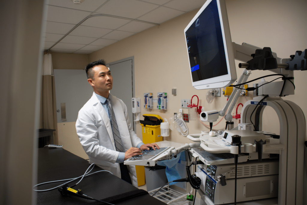 Doctor wears a white lab coat and stares intensely at screen on medical equipment while typing in information.